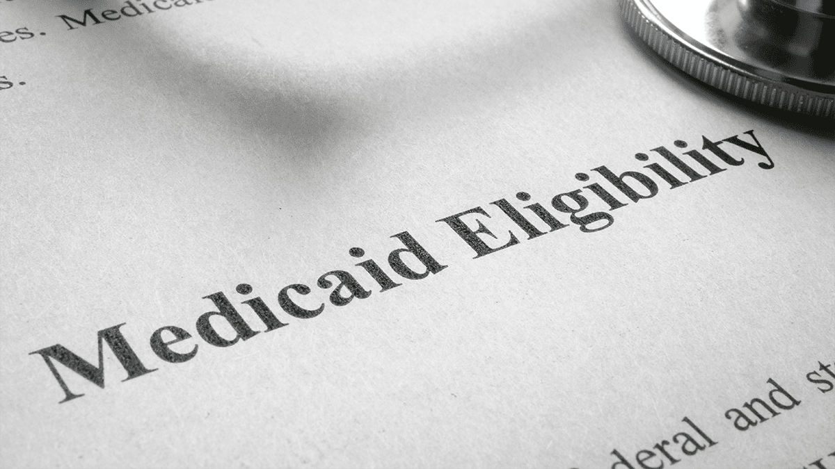 A black and white image of a Medicaid eligibility application form with a stethoscope laying diagonally across the top right corner of the page.