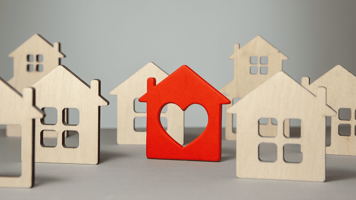 Wooden cutouts of homes for purchase or rent. In the center is a red house with a heart cut-out.