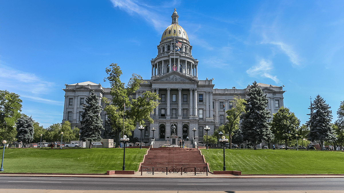 Picture of the Colorado Capitol building's front entrance with stairs leading up to the building and a clear sky day with green grass