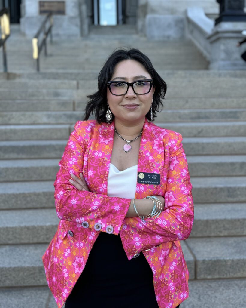 Representative Elizabeth Velasco in a pink and orange blazer in front of the Capitol steps