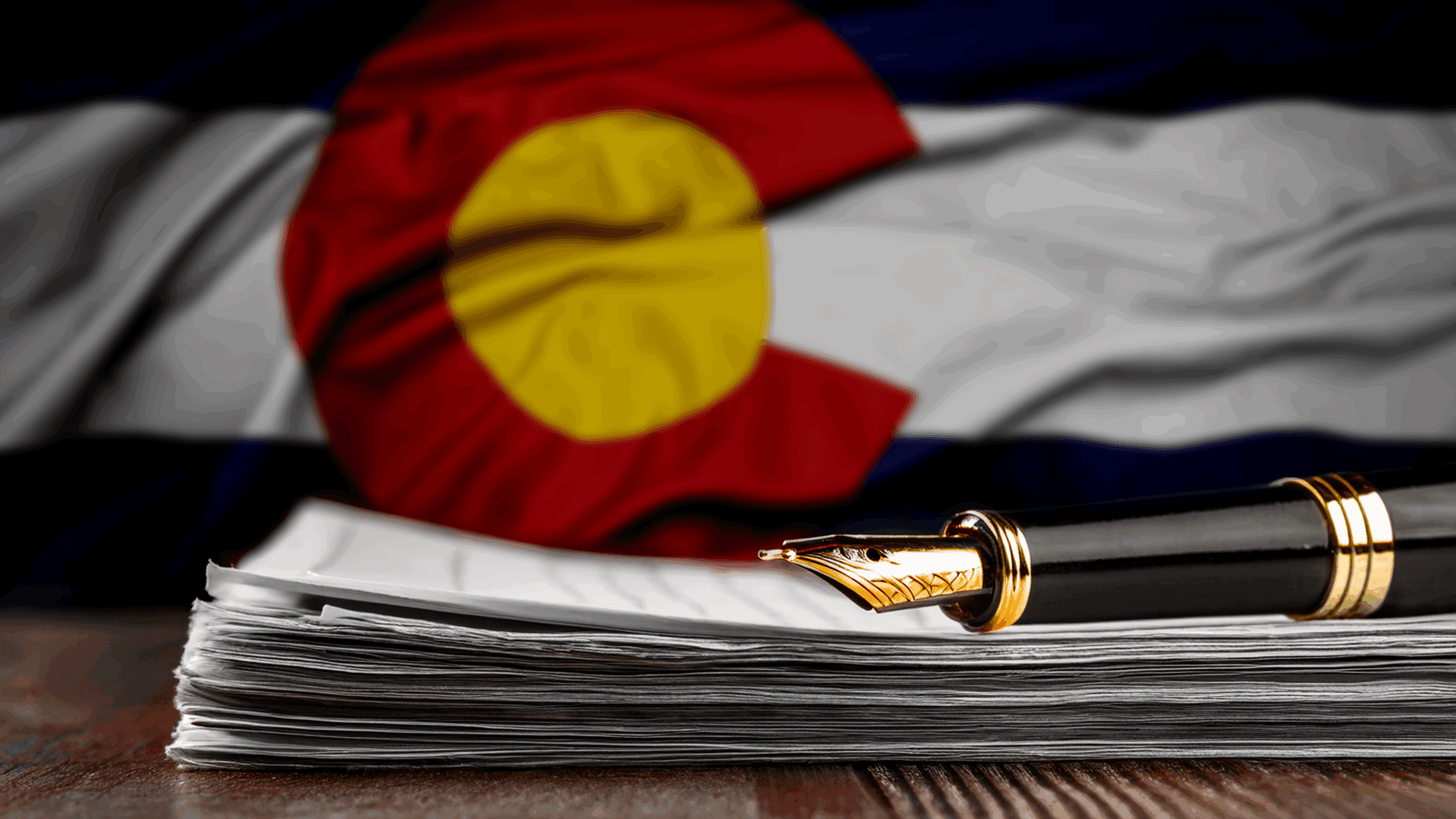 stock photo of a fountain pen on a stack of paper, in front of the Colorado flag.